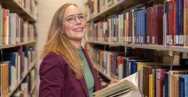 Porträt einer Frau, die im Gang einer Bibliothek steht