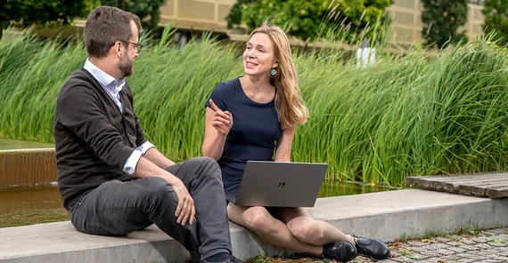 A woman and a man sit in front of a fountain and talk.