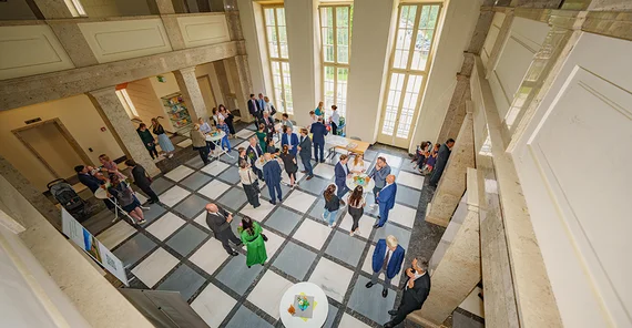 Blick in einen großen Raum von oben, in dem rund 30 Menschen stehen und miteinander reden
