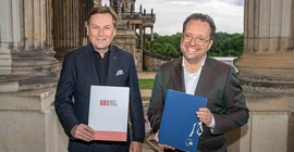 Zwei Männer zeigen Dokumentenmappen in die Kamera.