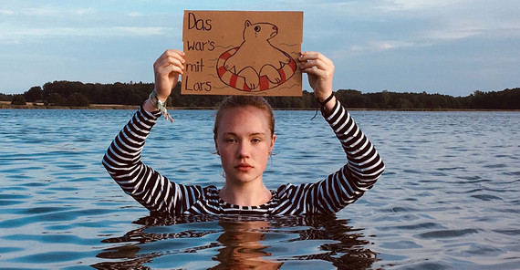 Lena Gundelfinger stieg für eine kreative Protestaktion in die Ostsee. Lena Gundelfinger steht in der Ostsee und hält ein Schild.