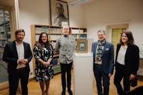 Fünf Menschen stehen um eine Vitrine mit einem Gemälde und schauen in die Kamera