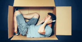 Foto: Adobe Stock/ master1305. Ein Mann sitzt in einem Karton.